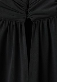 Vestido negro con escote fruncido y falda fluida. Hecho de una tela texturizada, con un brillo sutil y un detalle de apertura central.