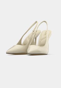 Escarpins à bride arrière en matériau ivoire brillant, avec un bout pointu et un talon élancé. Comprennent une semelle intérieure rembourrée et un design minimaliste.