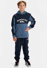 Mörkblå och ljusblå färgblockerad hoodie med känguruficka, med "Quiksilver"-logotyp i vitt. Matchas med mörkblå mjukisbyxor.
