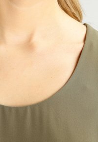 Olivgrön topp med en mjuk textur, med rundad halsringning och en enkel, ren design.