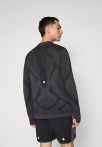 Long-sleeve dark gray sweatshirt featuring textured, abstract patterns and a reflective accent on the back, paired with black shorts.