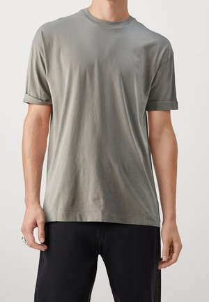 T-shirt in cotone grigio con scollatura rotonda, maniche corte arrotolate e vestibilità morbida, abbinato a jeans neri. Texture liscia.