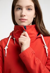 Giacca impermeabile rossa con colletto alto, coulisse bianche e hardware argentato. Tessuto liscio, parzialmente zipata davanti.