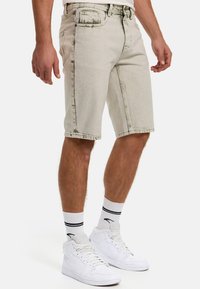 Lys grå denim shorts med et falmet design, skrå lommer og synlige syninger. Båret sammen med hvide høj-top sneakers og stribede sokker.