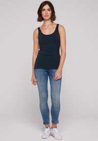 Camiseta sin mangas de color azul marino con escote redondeado, combinada con jeans ajustados de color azul claro y zapatillas blancas. Tejido suave, diseño entallado, detalles mínimos.