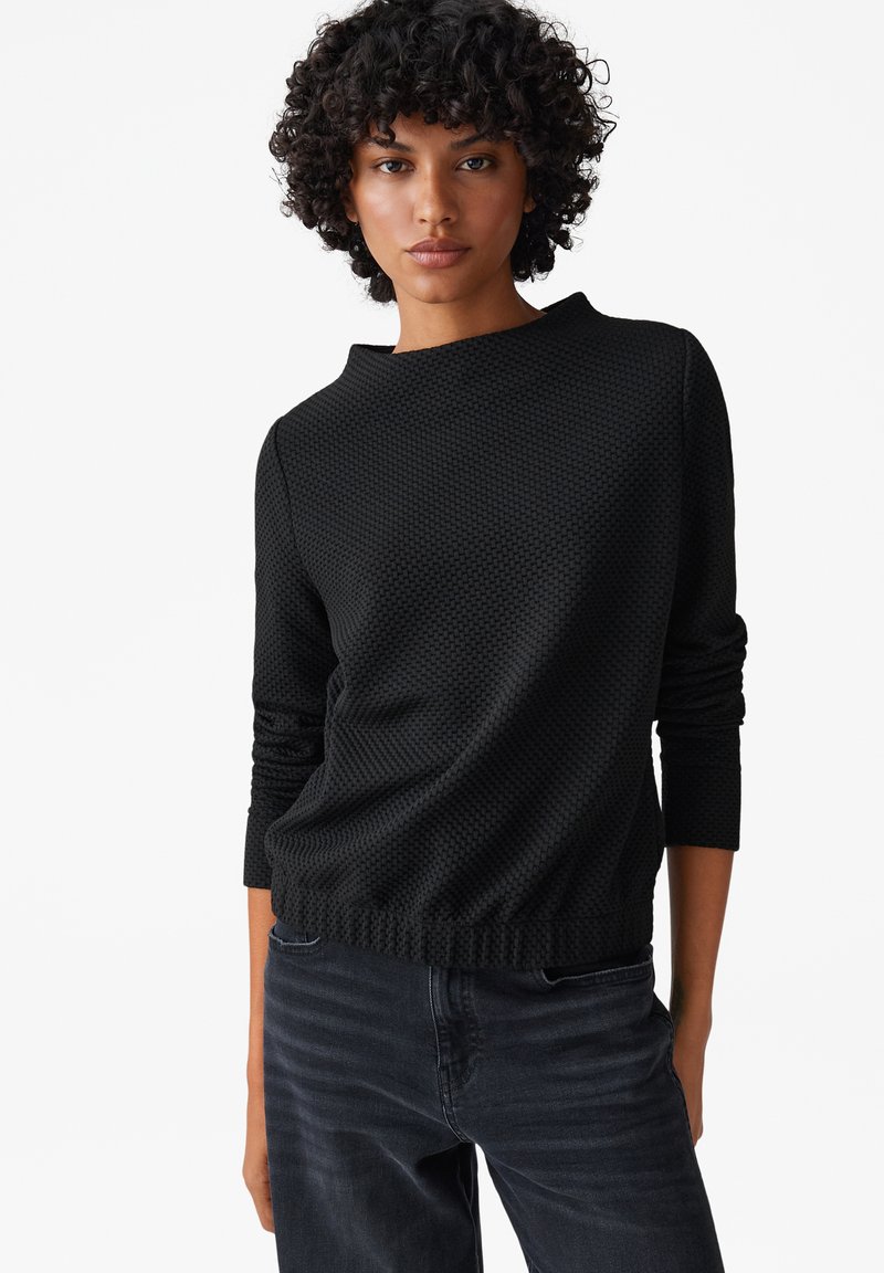 Maglione nero a trama con scollo rotondo e orlo a coste, con maniche lunghe e vestibilità rilassata, abbinato a jeans scuri.