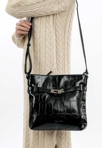 Borsa a tracolla nera in pelle con texture in pelle di coccodrillo, cinturino regolabile e hardware in metallo sul davanti per la chiusura.