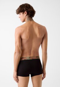 Boxer briefs neri con una fascia camouflage che presenta la scritta rossa "GUESS". Texture liscia, forma aderente e design minimalista.