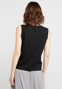 Top sans manches noir en coton doux, avec un col rond et une coupe décontractée, présenté de dos avec des cheveux texturés au premier plan.