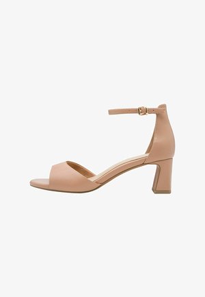 Sandales à talons en cuir nude avec bout ouvert, bride cheville avec boucle dorée, et talon bloc. Texture lisse et design minimaliste.