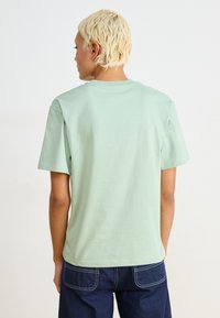 T-shirt in cotone verde menta con maniche corte e colletto a girocollo, caratterizzato da una texture liscia e una vestibilità comoda, indossato con jeans blu scuro.