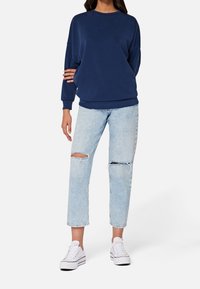 Felpa blu navy con colletto a girocollo, taglio oversized e maniche lunghe, abbinata a jeans strappati azzurri e sneaker bianche.