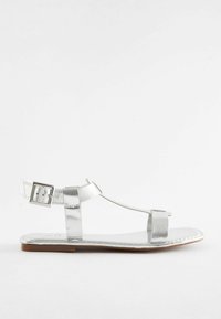 Silver metalliska sandaler med platt sula, justerbar vristrem och T-bar design. Slät yta med minimal detaljering.