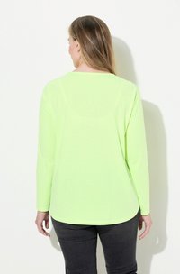 Langarmhemd in leuchtendem Limettengrün mit weicher Textur und abgerundetem hinten verlängertem Saum. Passt gut zu dunklen Jeans, die minimalistische Designelemente aufweisen.