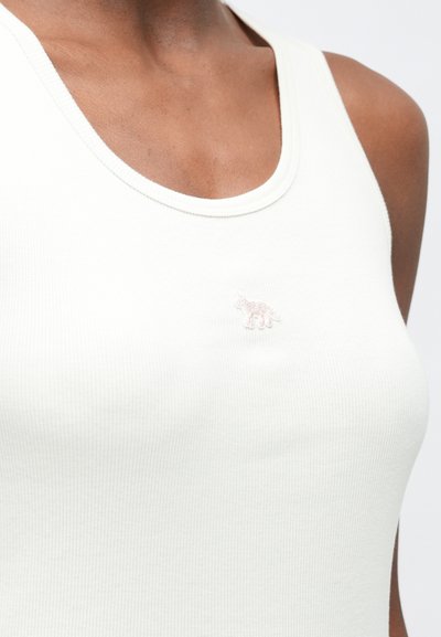 Biely rebrovaný tielko s okrúhlym výstrihom, na ľavej strane hrude s malým, svetloružovým vyšívaným logom zvieraťa.