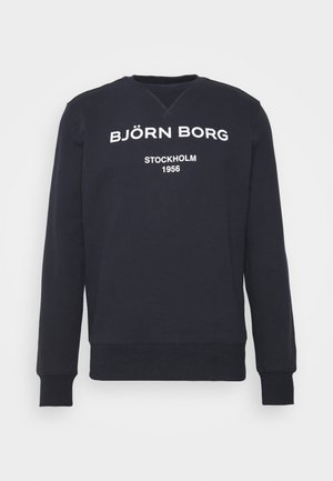 Sweat-shirt bleu marine col rond avec texte blanc "BJÖRN BORG" et "STOCKHOLM 1956" sur la poitrine, manches longues, poignets et bas côtelés.