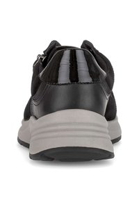 Achteraanzicht van een zwarte sneaker met een glanzende hak en een dikke grijze zool op een witte achtergrond