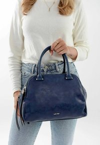 Marineblaue Handtasche aus strukturiertem Leder, mit kurzen Griffen, Reißverschluss und dekorativen Quasten. Logo auf der Vorderseite sichtbar.