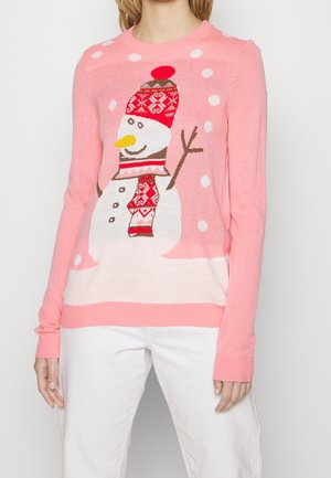 Personne portant un pull rose avec un bonhomme de neige portant un chapeau rouge à motifs et une écharpe, bras en forme de branches, entourée de points blancs de neige.
