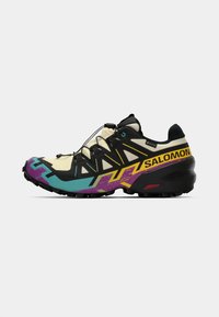 Chaussures de trail running avec une tige noire, des accents beiges et des motifs géométriques colorés. Dotées d'une semelle flexible et d'un système de laçage rapide.