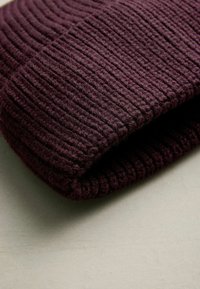 Knit beanie in deep burgundy, featuring a ribbed texture. The fabric appears soft and warm, with a folded cuff design.