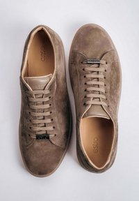 Para brązowych niskich sneakersów z zamszu z beżowymi sznurowadłami, metalowymi końcówkami z logo oraz jasnobrązową wkładką na białym tle.