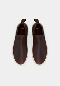 Hnědé kožené nazouvací boty s elastickými postranními panely a bílými gumovými podrážkami, s hladkou texturou a minimalistickým designem.