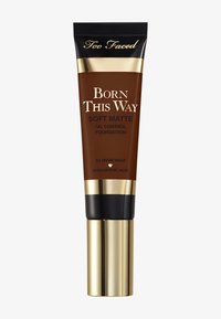 Foundation tube with a brown body, gold accents, and black cap. Text: "Born This Way Soft Matte Oil Control Foundation." 24-hour wear.