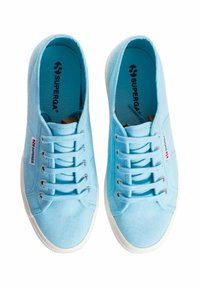 Sneakers di tela azzurro chiaro con suole in gomma bianca, dotate di sei asole, una parte superiore testurizzata e una piccola etichetta con logo rosso sul lato.