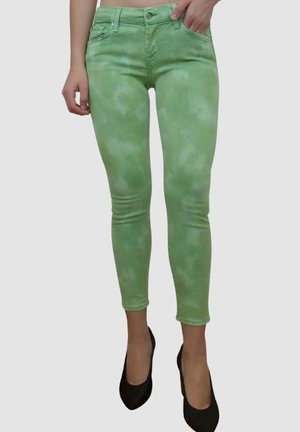 Jeans verde claro con un patrón de tie-dye, diseño de cintura alta, cinco bolsillos y un ajuste ceñido, combinados con zapatos de tacón negro.