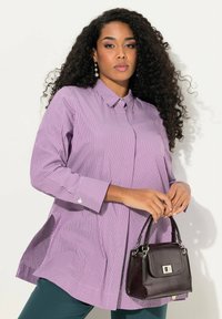 Paarse en witte gestreepte blouse met lange mouwen en een kraag, voorzien van zijopeningen. Gecombineerd met een kleine donkere handtas met zilverkleurige hardware.