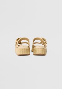 Tan sandals with a woven texture, featuring a high platform, adjustable ankle strap, and a round buckle accent.