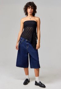 Black lace strapless top paired with dark blue wide-leg denim shorts. Model wears white socks and black shoes, standing on a plain background.