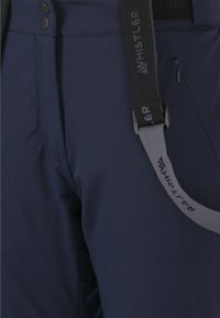 Marina snöbyxor gjorda av slät, vattenresistent tyg med ett vertikalt band märkt "WHISTLER," med knappar och en ficka med dragkedja.