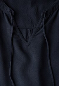 Navyblauw, lichtgewicht stoffen top met een V-halsontwerp, trekkoorden bij de halslijn en een subtiel textuurpatroon door het hele stuk.