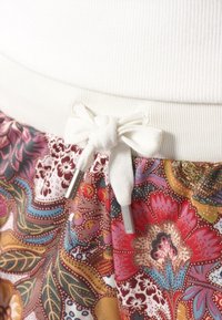 Květinové kraťasy s bílým žebrovaným pasem, který je ozdoben mašlí a dvěma kovovými koncovkami na stahovací šňůrce pro úpravu velikosti.