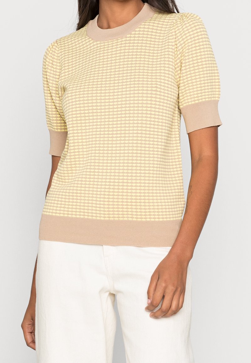 Krótki rękaw, lekki sweter typu pulower w jasnym żółtym kolorze z teksturowanym wzorem oraz beżowym prążkowanym kołnierzem i dołem. Gładki materiał, dopasowany krój.