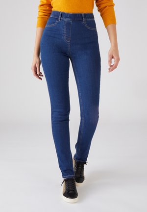 Jeans in denim blu a vita alta con una vestibilità slim, caratterizzati da una texture liscia e dettagli di cucitura discreti, abbinati a sneakers nere.