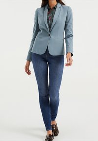 Lichtblauwe op maat gemaakte blazer met opgezette revers, gecombineerd met donkerblauwe skinny jeans. De blazer heeft een gestroomlijnd ontwerp en een knoopsluiting aan de voorkant.
