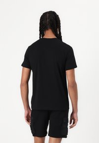 T-shirt en coton noir à manches courtes et coupe classique, avec une texture lisse et un design minimalist. Encolure structurée.