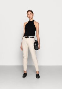 Top preto sem mangas com textura canelada, calças justas em tom creme, cinto preto com fivela redonda, mala preta e mocassins pretos.