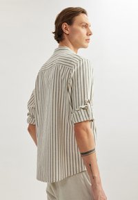 Gestreepte lange mouwen blouse in beige en marineblauw, gemaakt van lichtgewicht stof. Heeft omrolbare mouwen en een gebogen zoom, met een rugpas detail.