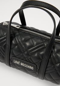Borsa a tracolla in pelle nera trapuntata con doppi manici, zip argento e una placca "LOVE MOSCHINO". Caratterizzata da una forma cilindrica compatta.