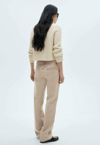 Maglione corto a coste beige abbinato a pantaloni beige a palazzo, con cuciture delle tasche sottili e una texture del tessuto liscia. Scarpe nere.