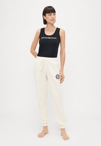 Čierny tielko s bielym logom "Emporio Armani", skombinované s krémovými teplákmi so čiernym kruhovým logom a elastickým pásom.