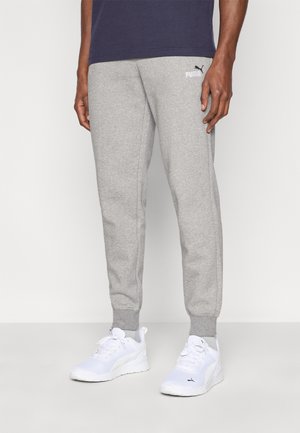 Pantaloni della tuta grigio chiaro in tessuto morbido, con vita e polsini elasticizzati, con un logo Puma nero vicino alla tasca. Scarpe da ginnastica bianche.