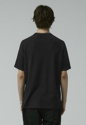 Black textured T-shirt with short sleeves and a crew neck, featuring a relaxed fit and minimal seams at the shoulders and back.