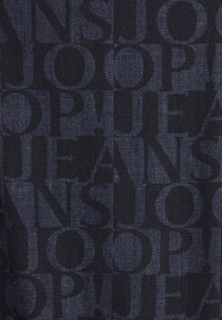 Tessuto in denim scuro con un motivo ripetuto di lettere in grassetto e scure che scrivono "JOOP! JEANS" in varie orientazioni e dimensioni.