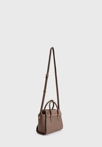 Bolso de cuero marrón con correa de hombro ajustable y dos asas cortas, de pie sobre un fondo liso gris claro.