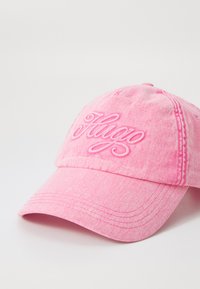 Rosa bomullsmössa med broderad "Hugo" i matchande rosa. Har en böjd skärm och sex paneler, med en texturerad, urblekt finish.